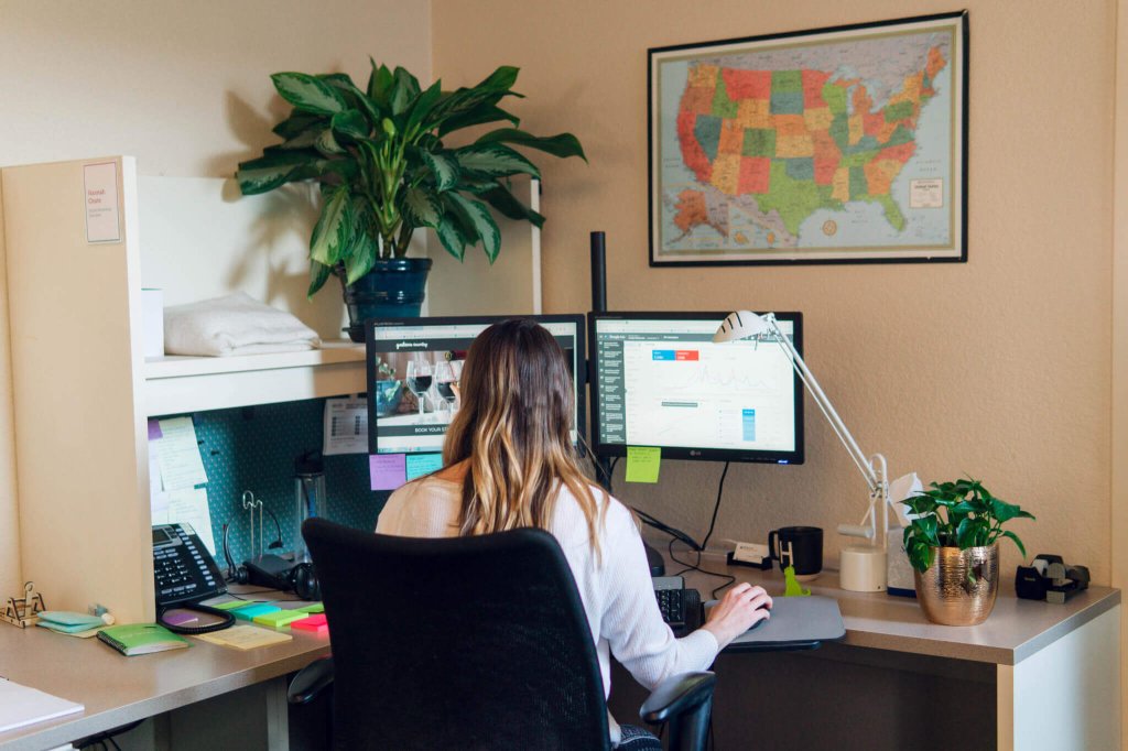 A woman working at her desk with dual monitors and a map on the wall