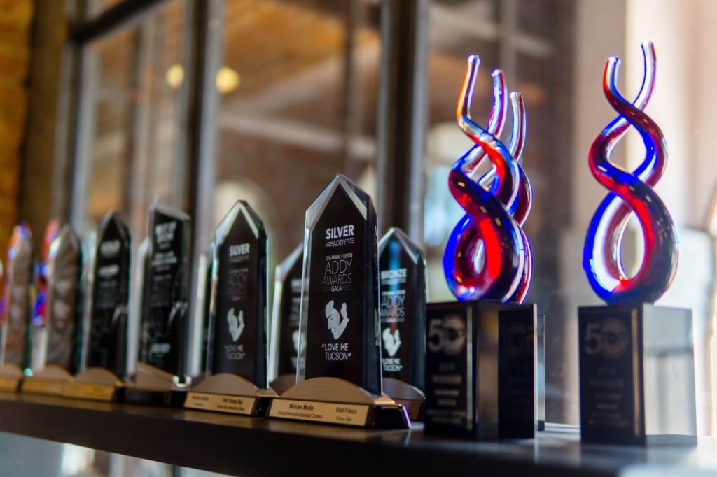 A row of various Addy awards displayed on a shelf