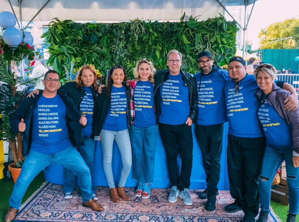 A group of people wearing matching blue t-shirts standing in front of a green wall