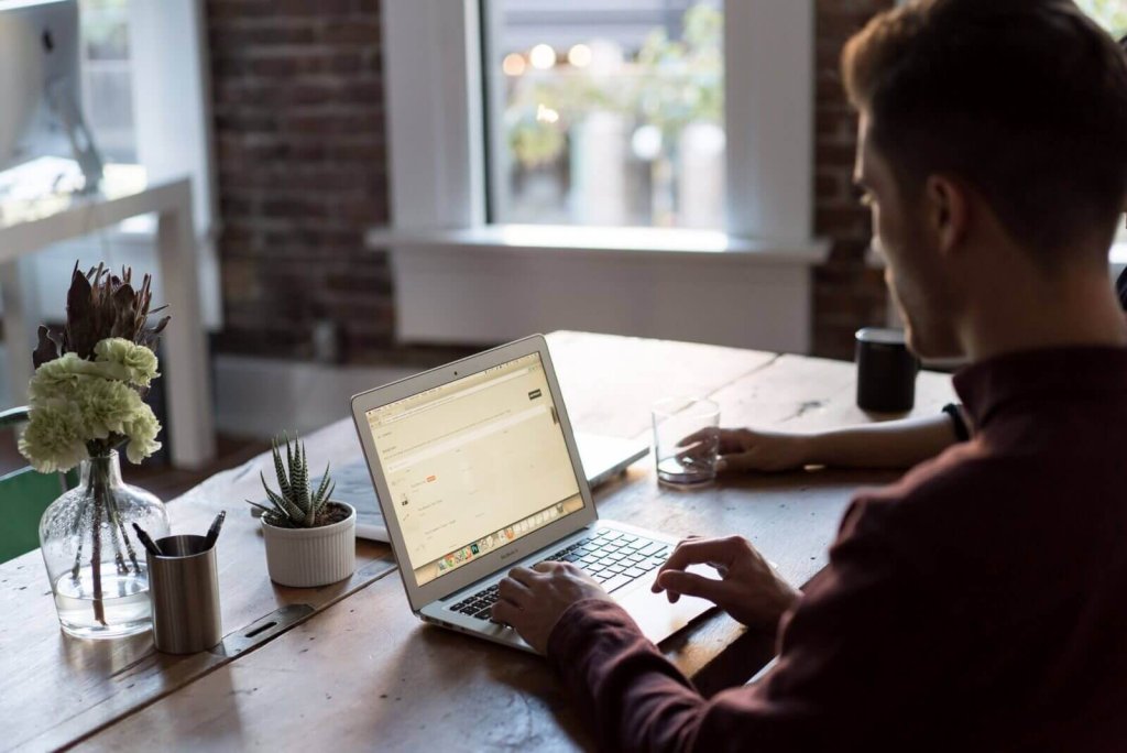 A man working on a laptop at a wooden table in a bright office
