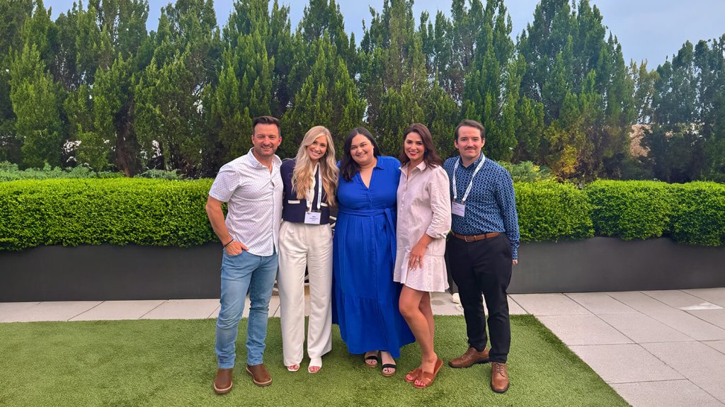 Five people standing together outdoors in front of a hedge
