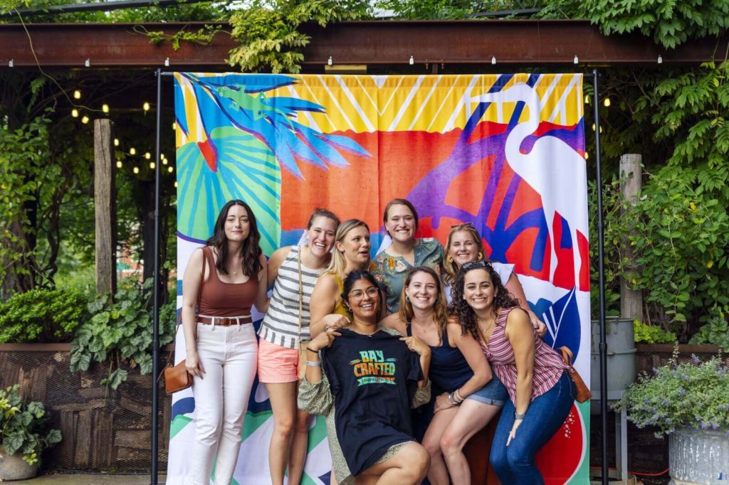 A group of eight young women smiling together in front of a colorful backdrop
