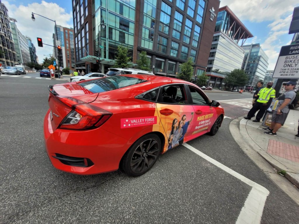 A red car with promotional branding parked on a city street corner