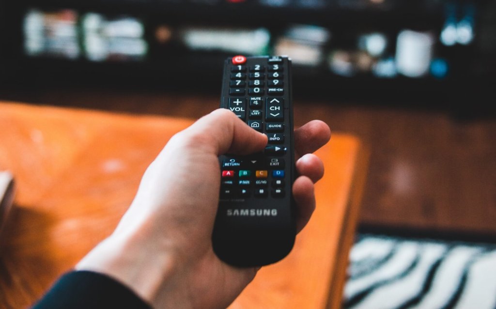 A hand holding a black Samsung television remote control in a living room
