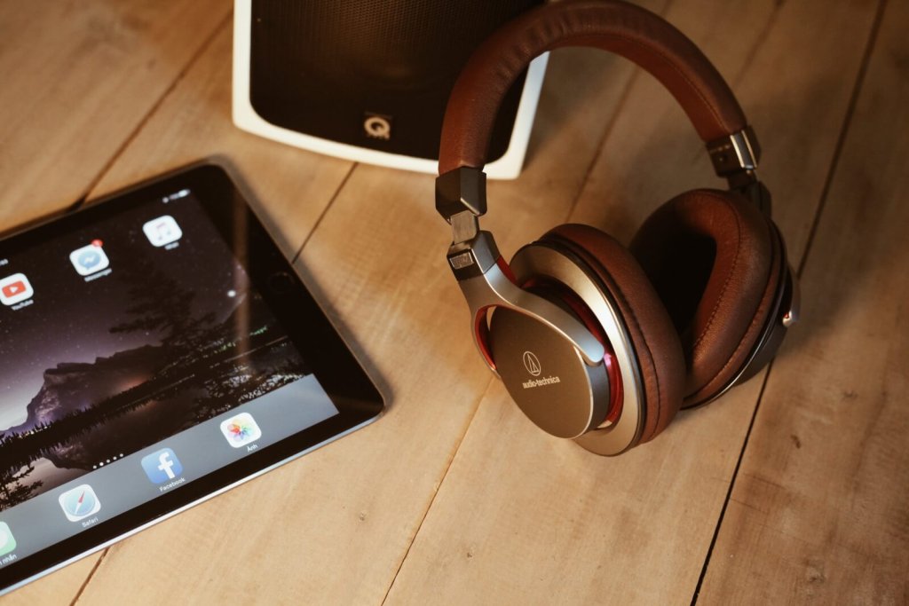Audio-Technica headphones, a tablet, and a speaker on a wooden surface