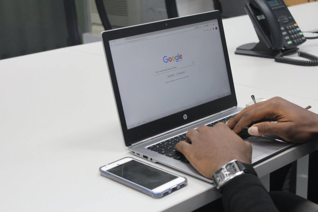 A person typing on an HP laptop displaying the Google search engine homepage