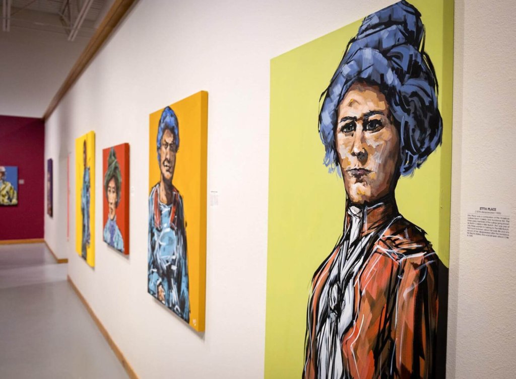 A series of colorful portrait paintings displayed on a white gallery wall