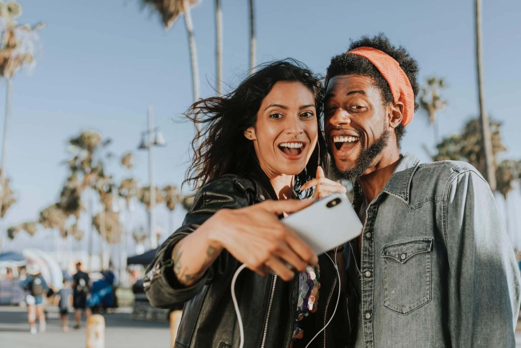 A happy couple taking a selfie together outdoors with palm trees in the background