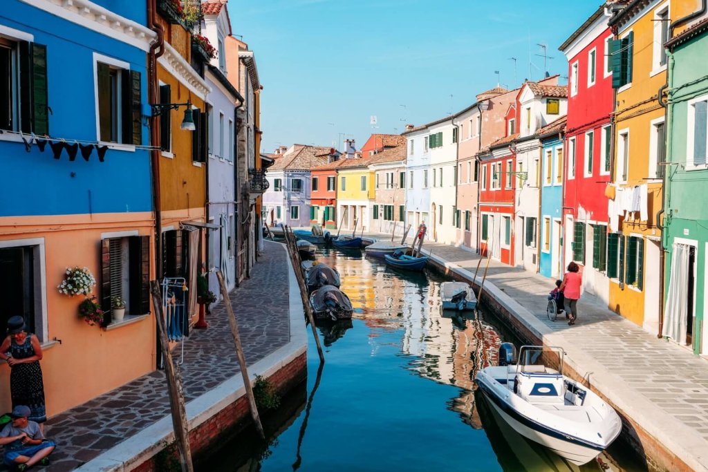 A scenic canal lined with vibrant, multi-colored houses and small boats in Burano, Italy