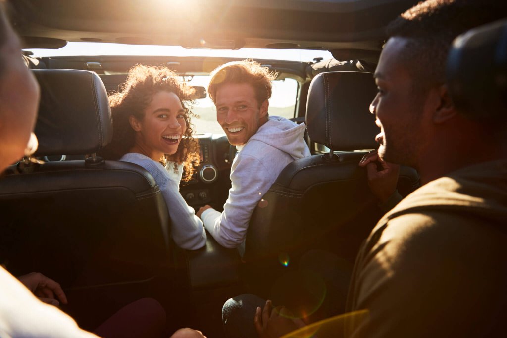 A group of friends smiling while riding in a car during sunset