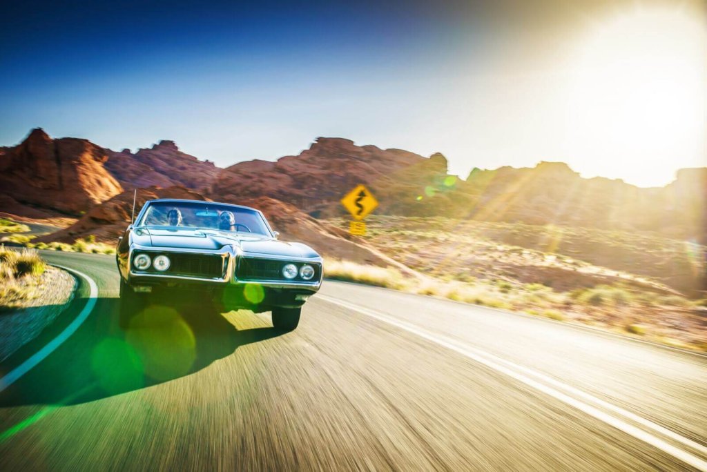 A vintage convertible car driving on a desert road at sunset