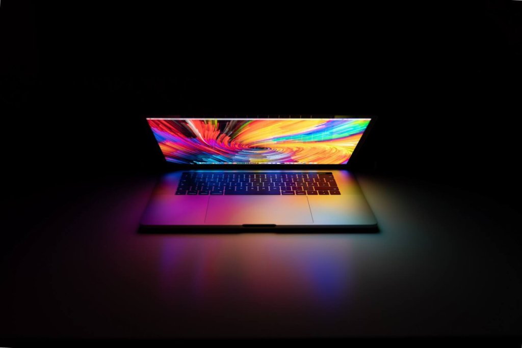 A laptop with a vibrant, colorful abstract screen glowing in a dark room