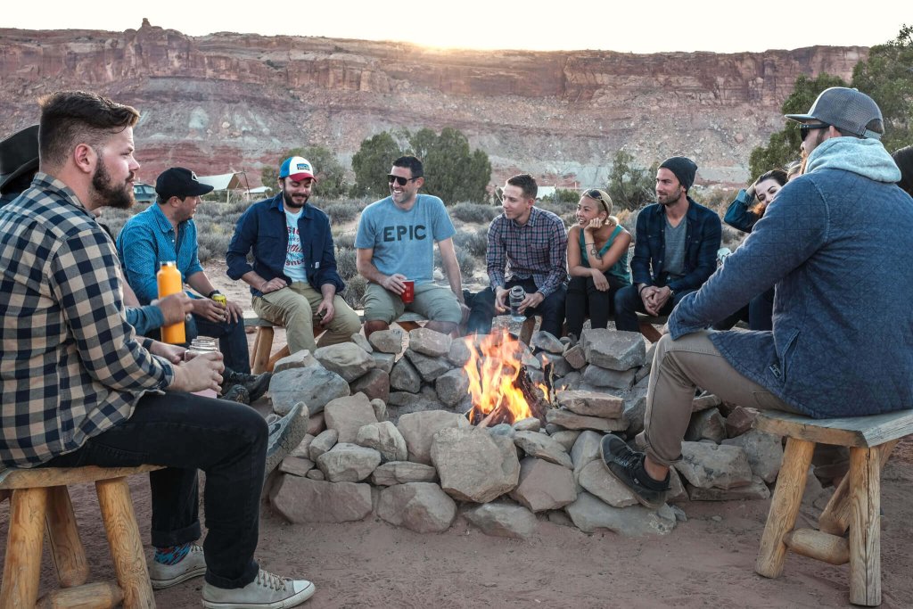 A group of friends sitting around a campfire in a desert landscape at sunset