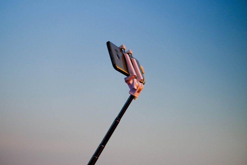 A smartphone mounted on a selfie stick against a clear blue sky