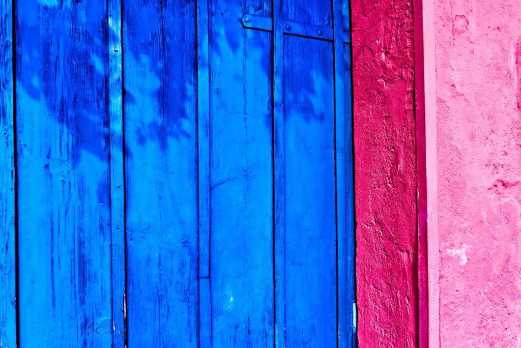 A bright blue wooden door set against a vibrant pink textured wall