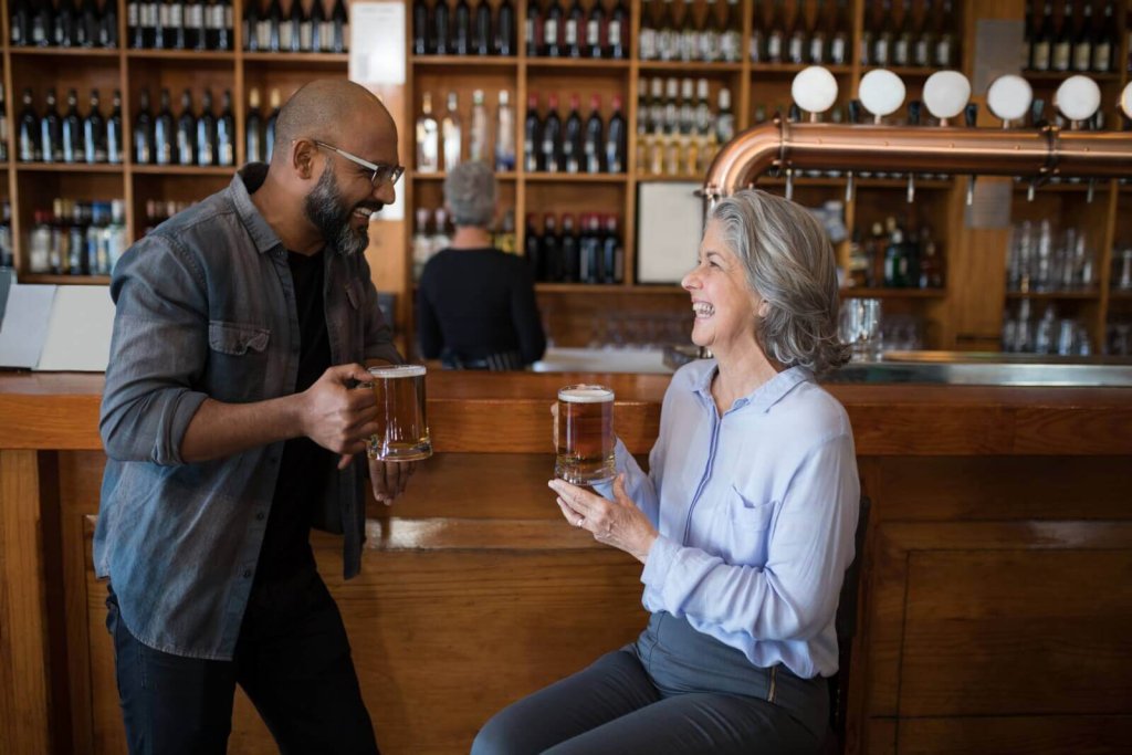 A man and a woman laughing while holding beer mugs at a bar
