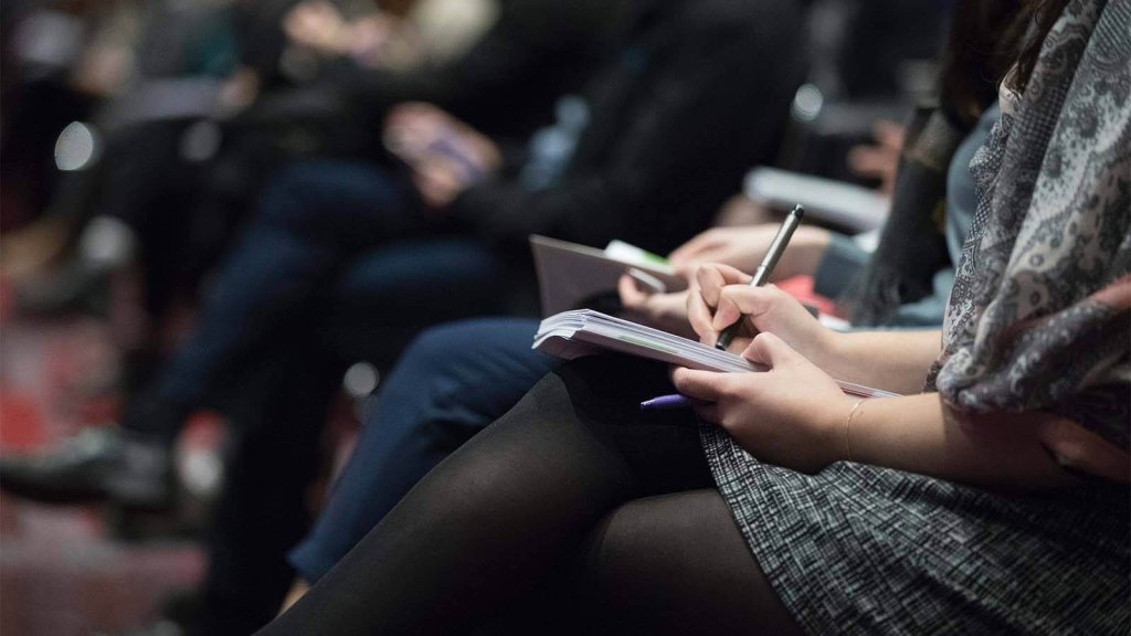 A person taking notes in a notebook during a conference or seminar