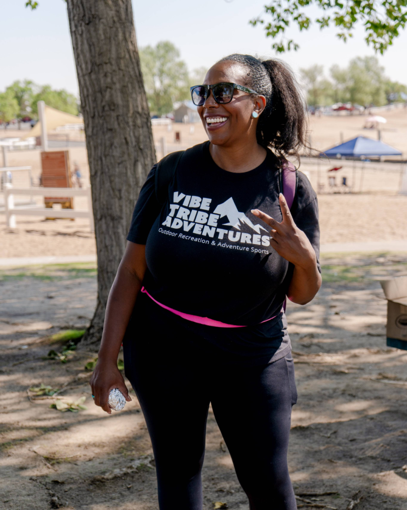 A smiling woman in a black shirt makes a peace sign outdoors