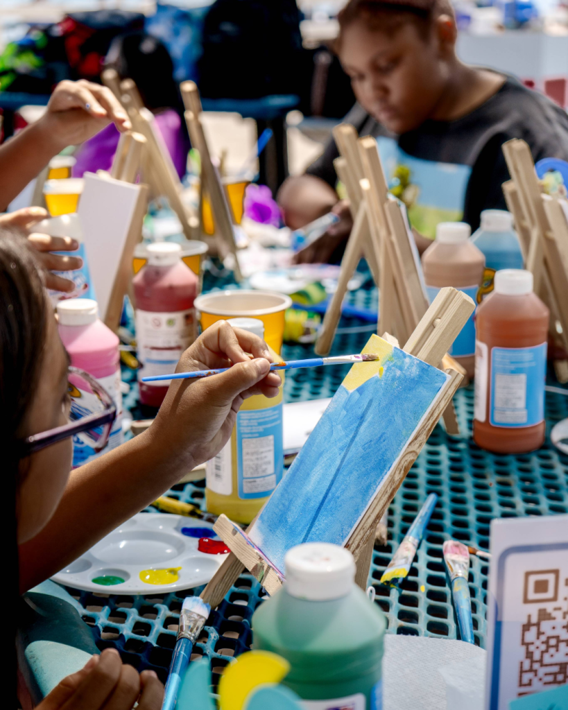 A group of children painting on small canvases at a table with art supplies