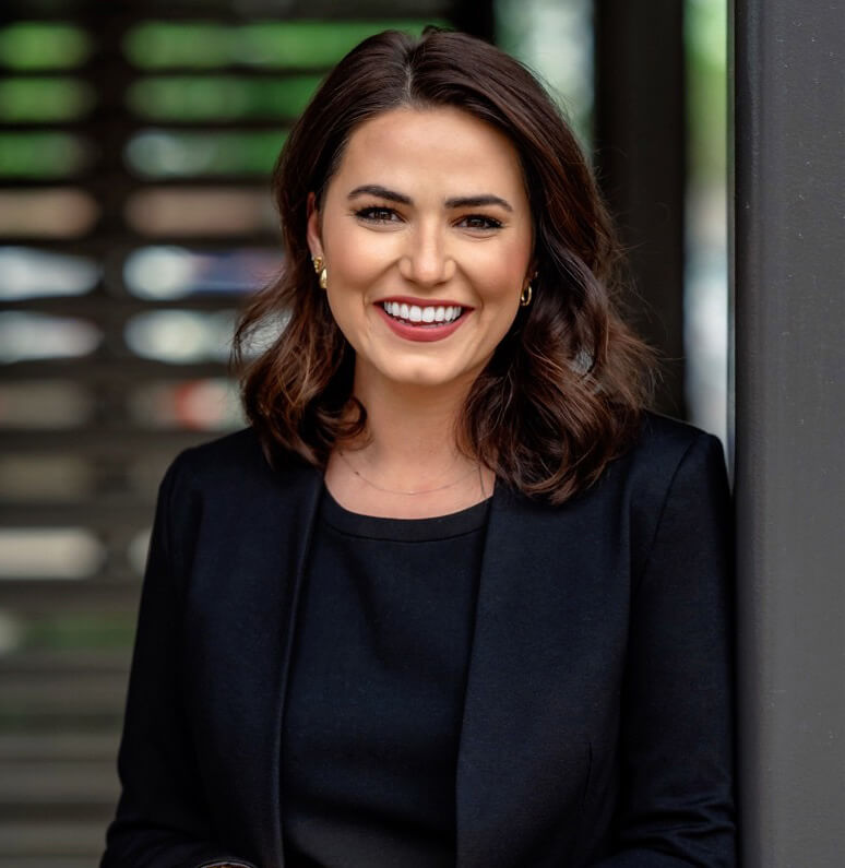 A smiling woman with dark hair wearing a black top and blazer