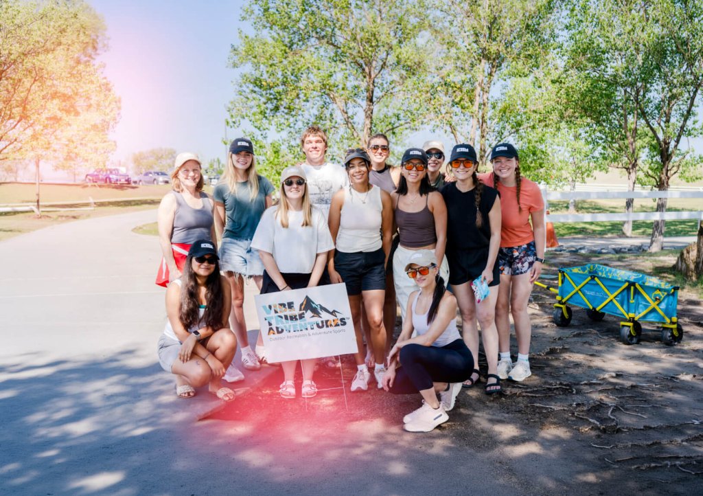 A group of people posing with a Vibe Tribe Adventures sign outdoors