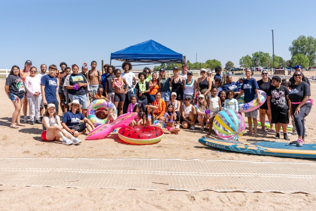 A large group of people posing together on a sandy beach with pool floats