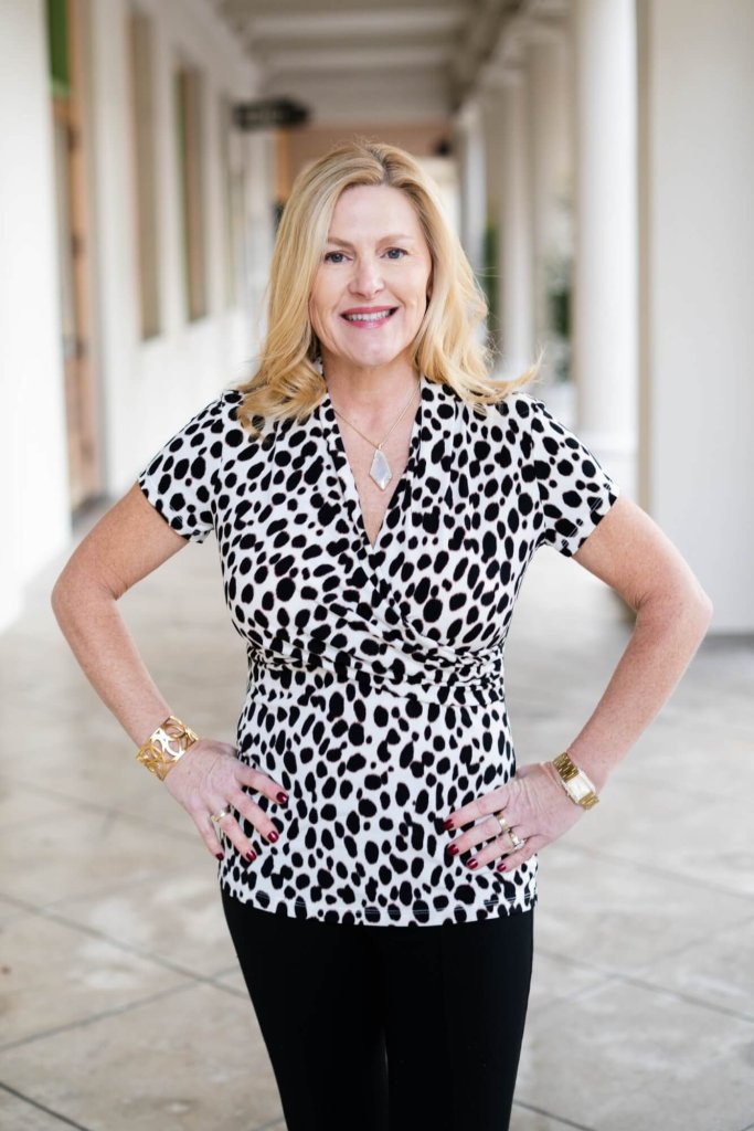 A smiling woman in a black and white spotted top with hands on hips