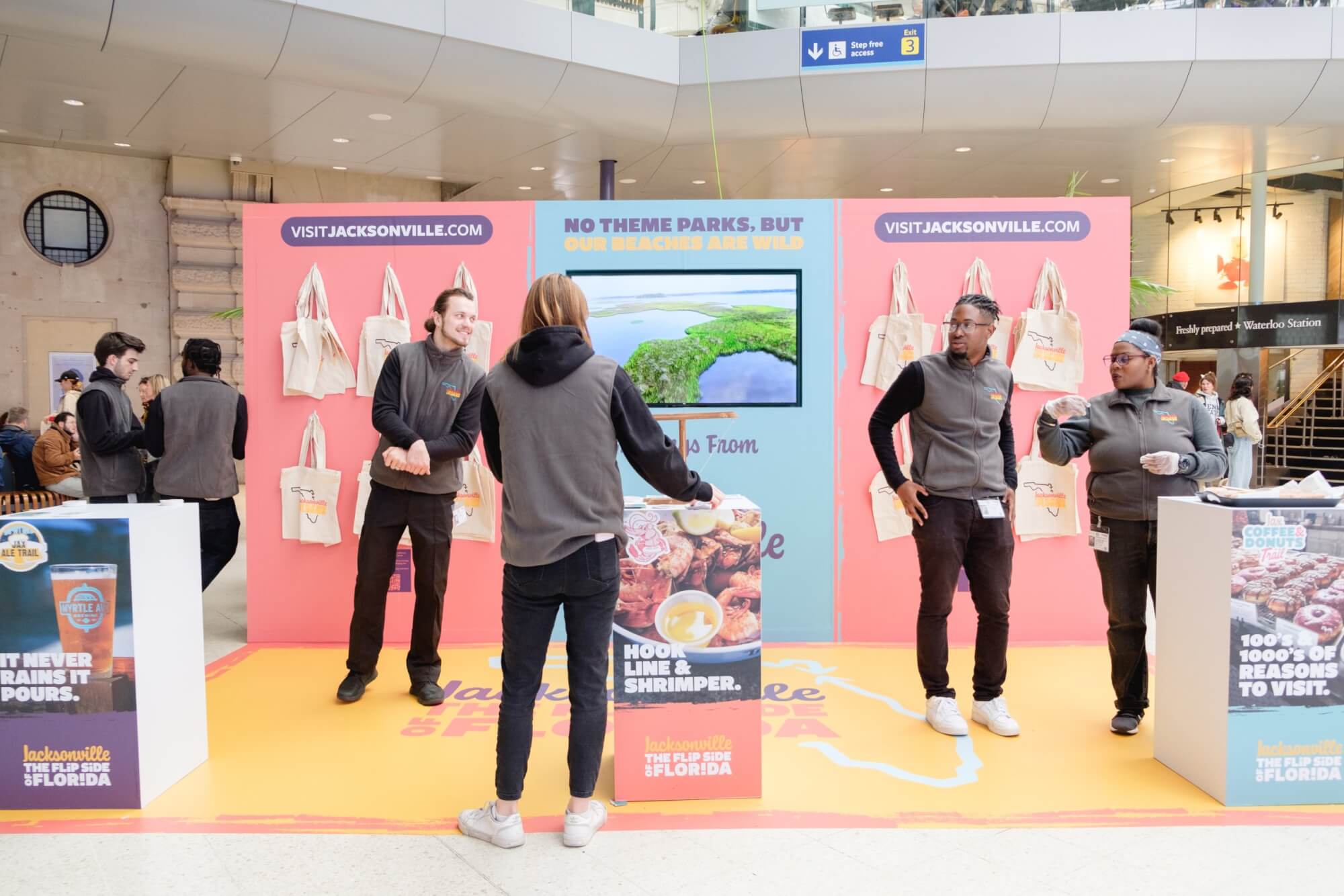 People in grey vests staff a colorful Jacksonville, Florida promotional booth with tote bags