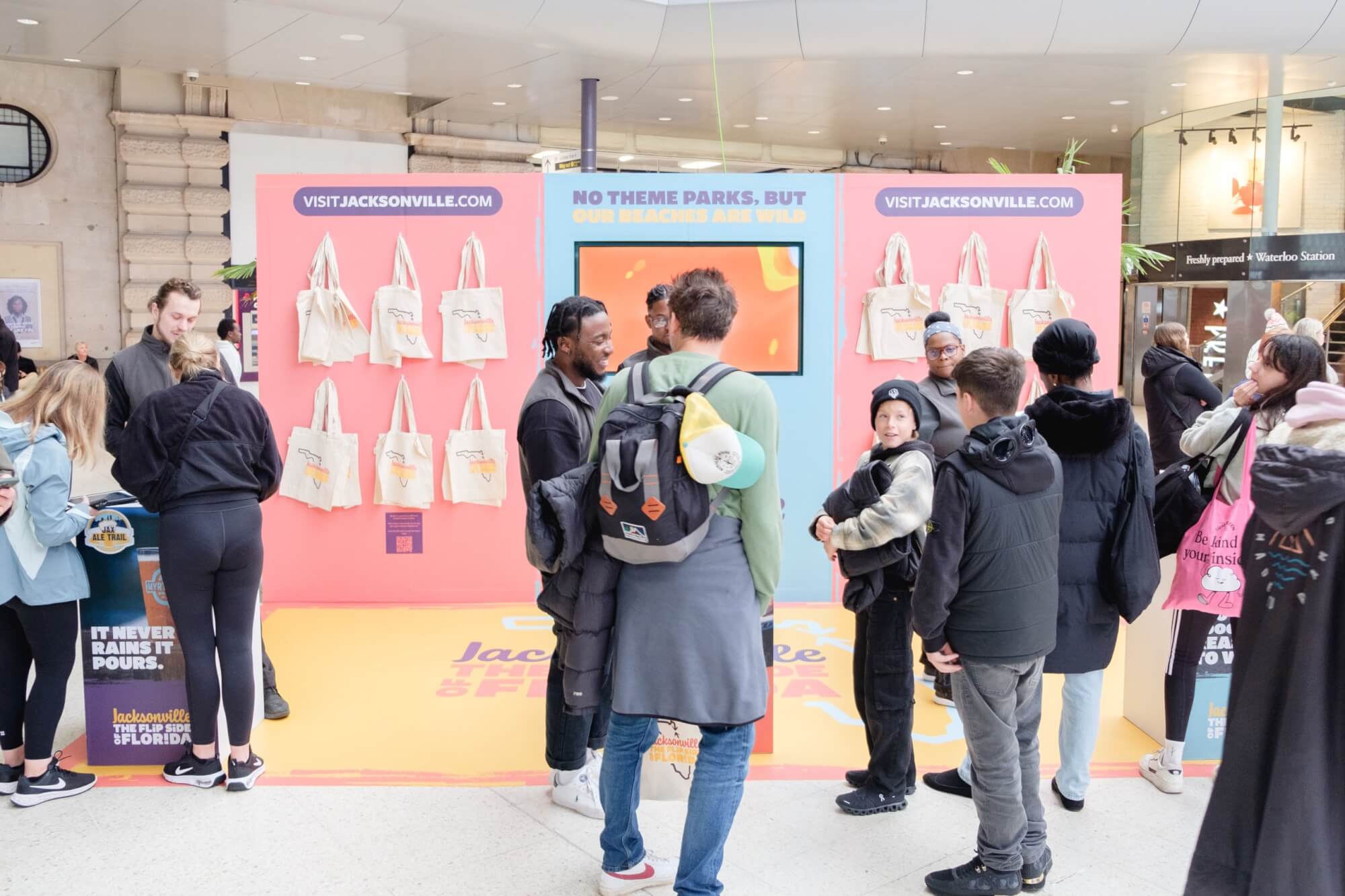 People gather around a colorful Jacksonville, Florida promotional booth with tote bags