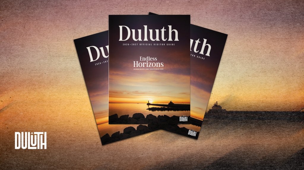 Three copies of the 2026-2027 Duluth official visitor guide featuring a sunset lighthouse scene