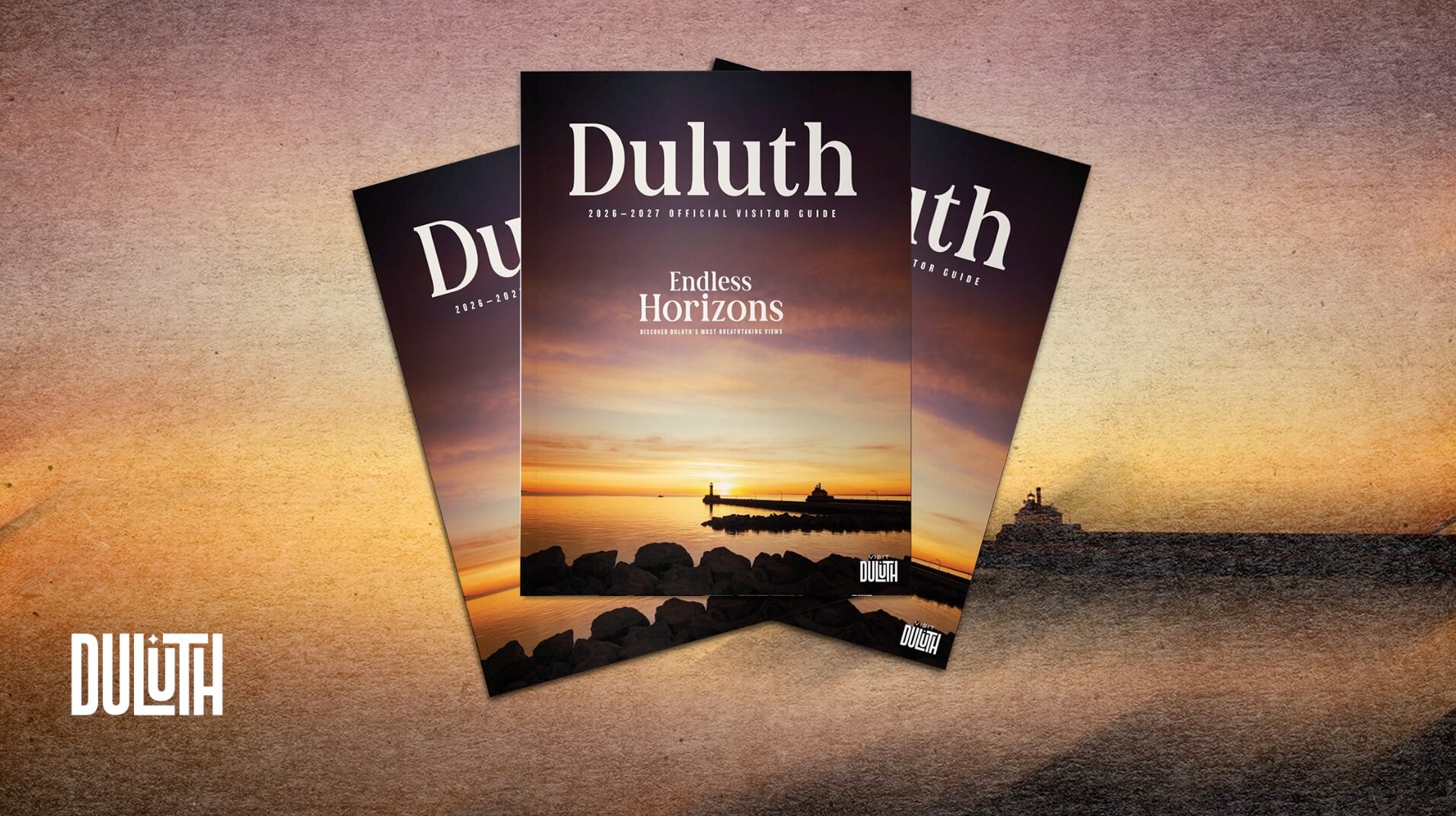 Three copies of the 2026-2027 Duluth official visitor guide featuring a sunset lighthouse scene