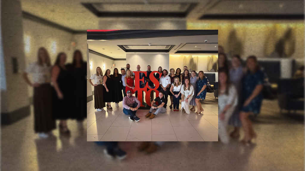 A large group of people posing for a photo behind a red ESTO sign