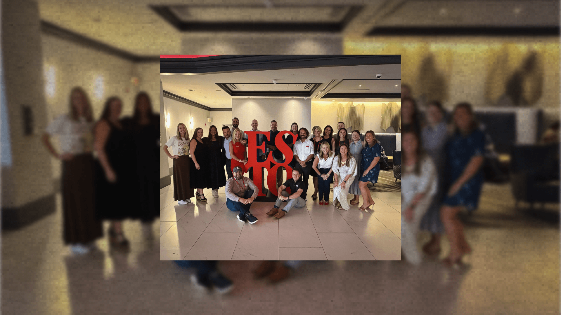 A large group of people posing for a photo behind a red ESTO sign
