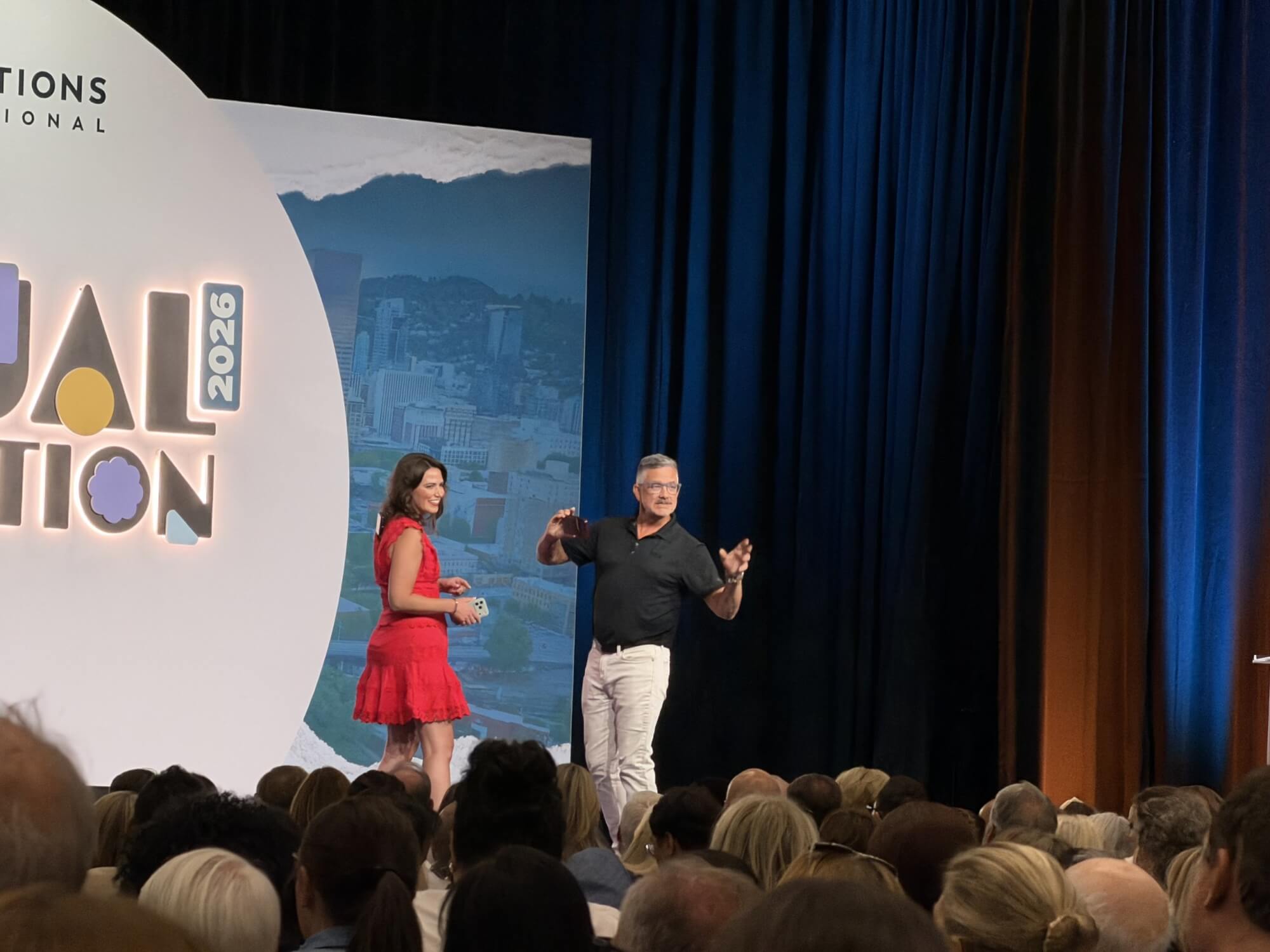 Two presenters on stage in front of a large audience at a conference