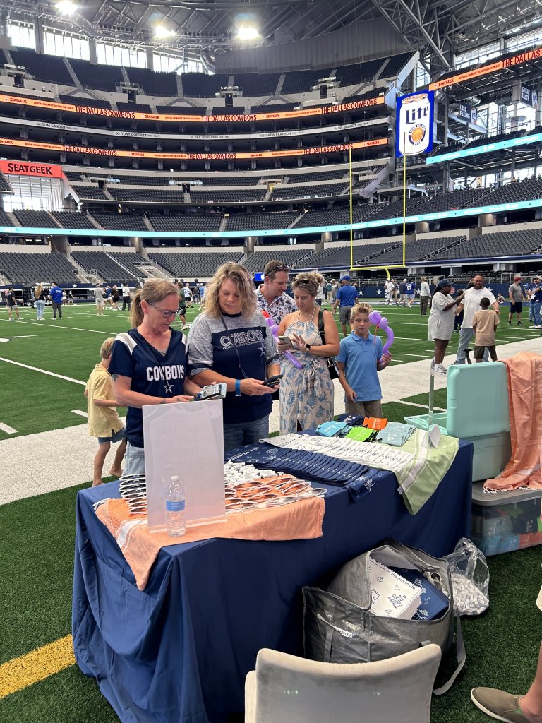 People gather around a table with merchandise on a football field inside a stadium