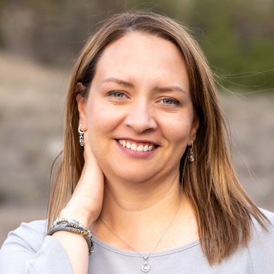 A smiling woman with shoulder-length brown hair poses for a portrait outdoors
