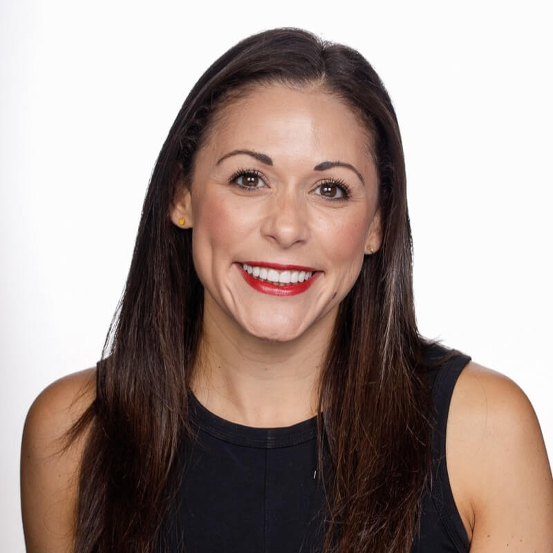 A smiling woman with long brown hair wearing a black top against white background