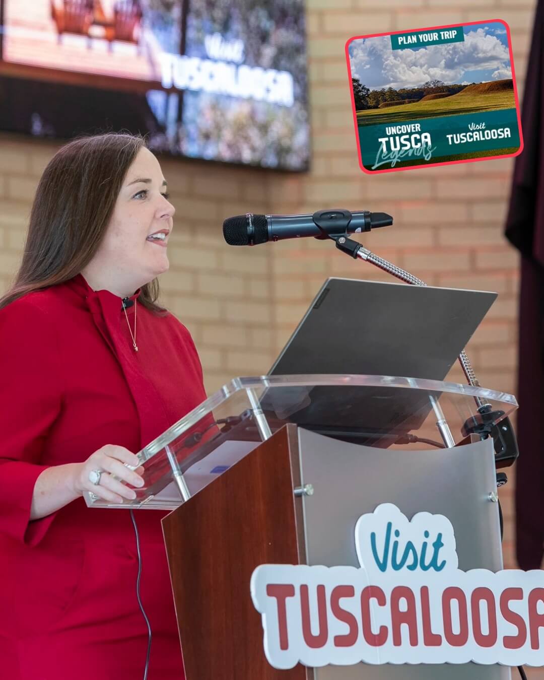 A woman in a red dress speaking at a podium with Tuscaloosa branding