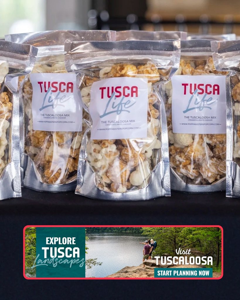 Several clear bags of Tusca Life popcorn displayed on a table with promotional signage