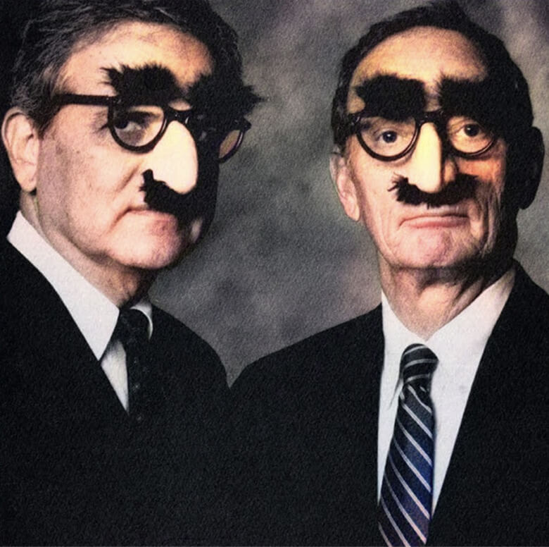 Two men in suits wearing Groucho Marx glasses with fake noses and mustaches